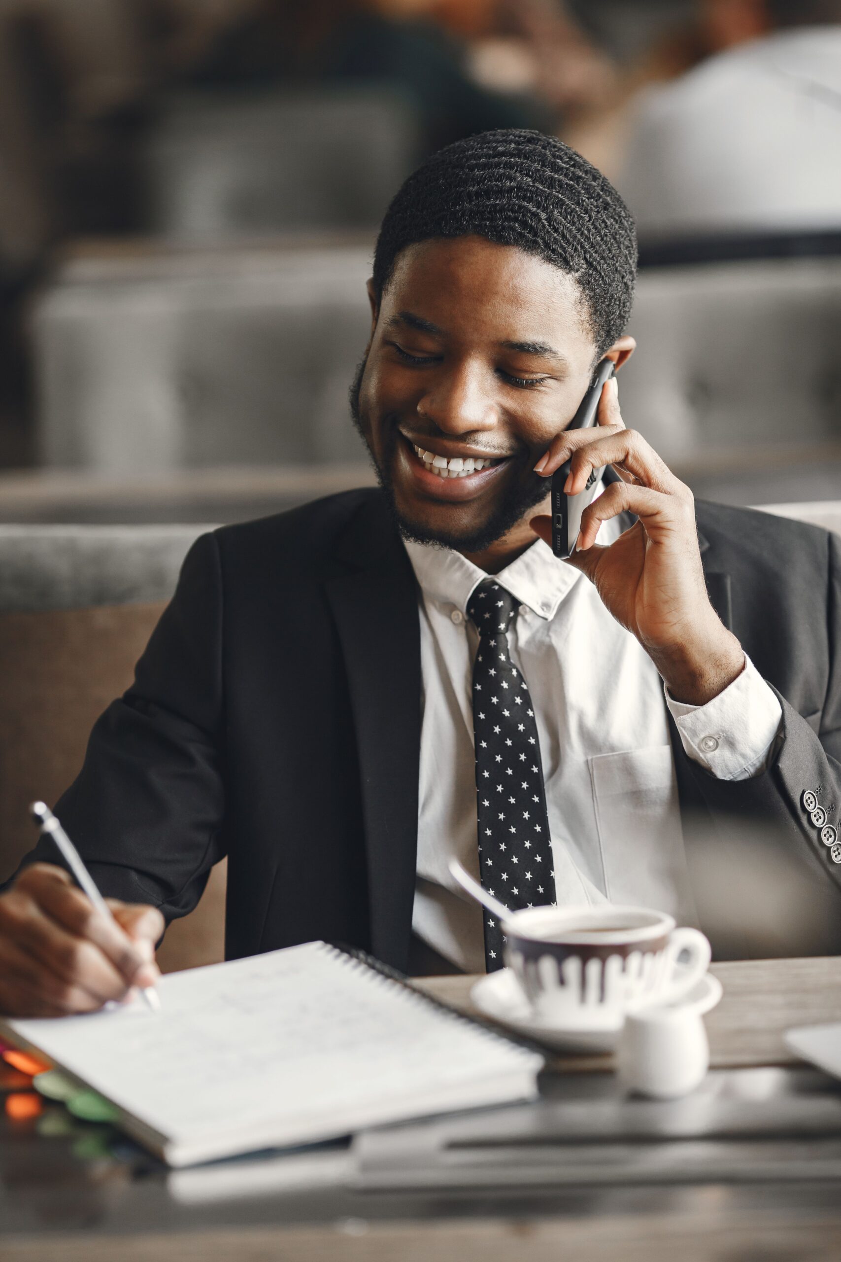 Smiling businessman talking on phone while taking notes in a modern office setting.